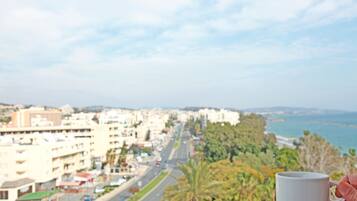 Vista de una ciudad con una carretera que lleva a una playa, una palmera y una taza blanca sostenida por una mano.