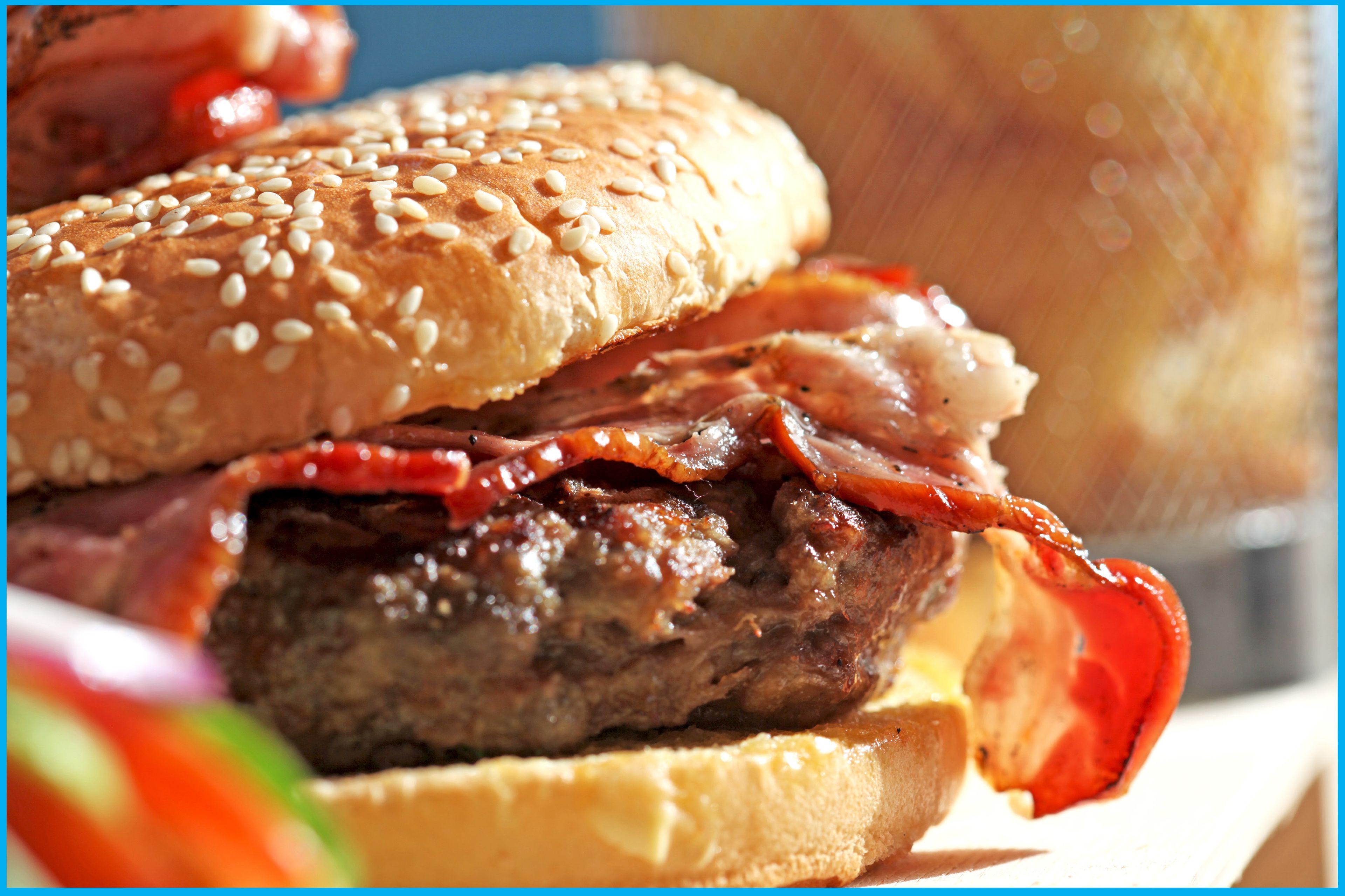 A close-up of a burger with sesame seed bun, bacon, and a beef patty.