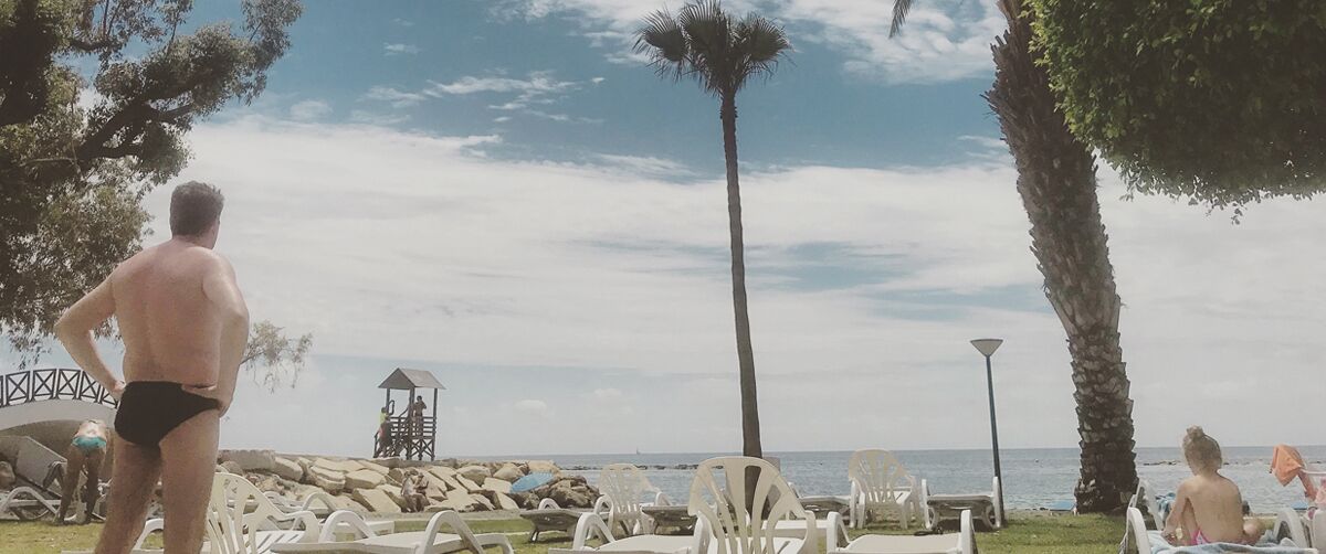 A beach with lounge chairs, a lifeguard tower, and palm trees.