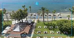 An aerial view of a beachside resort with palm trees, sun loungers, and a gazebo.