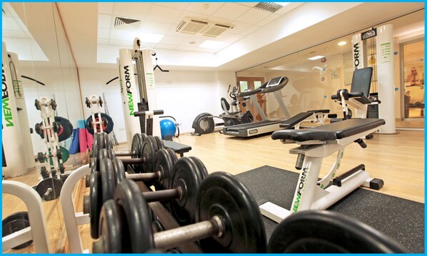 A gym with various exercise equipment, including dumbbells, a bench, and cardio machines.