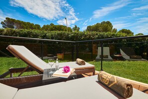 A sunlit outdoor lounge area with a glass balustrade, a reclining chair, a small table with a book and a glass, and a towel with a logo. - Protur Turó Pins Hotel (Capdepera)