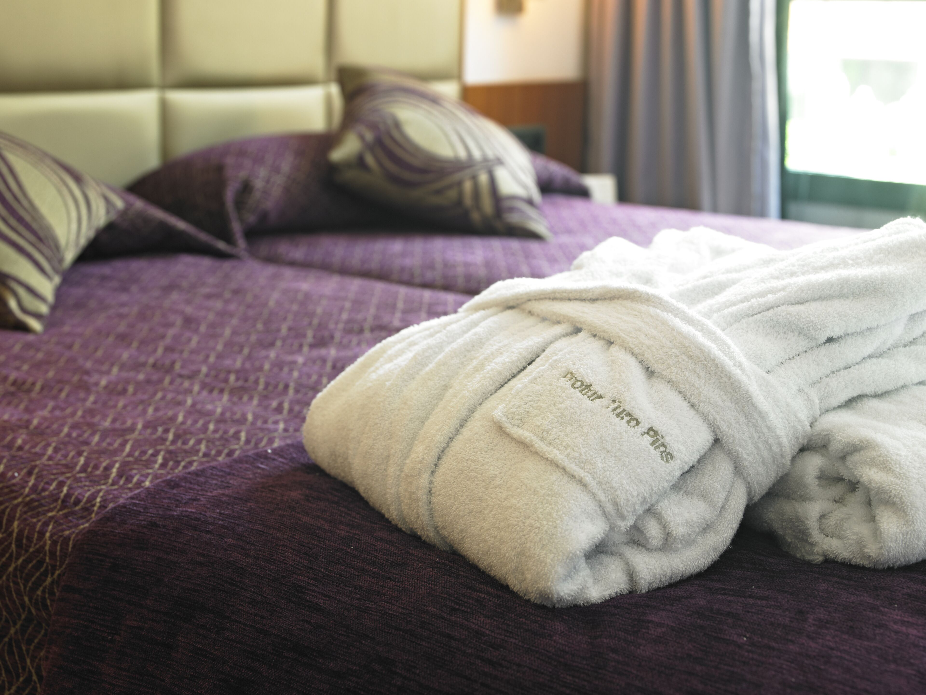 Un lit bien fait, recouvert d’une couverture violette, avec un peignoir blanc posé sur le dessus.
