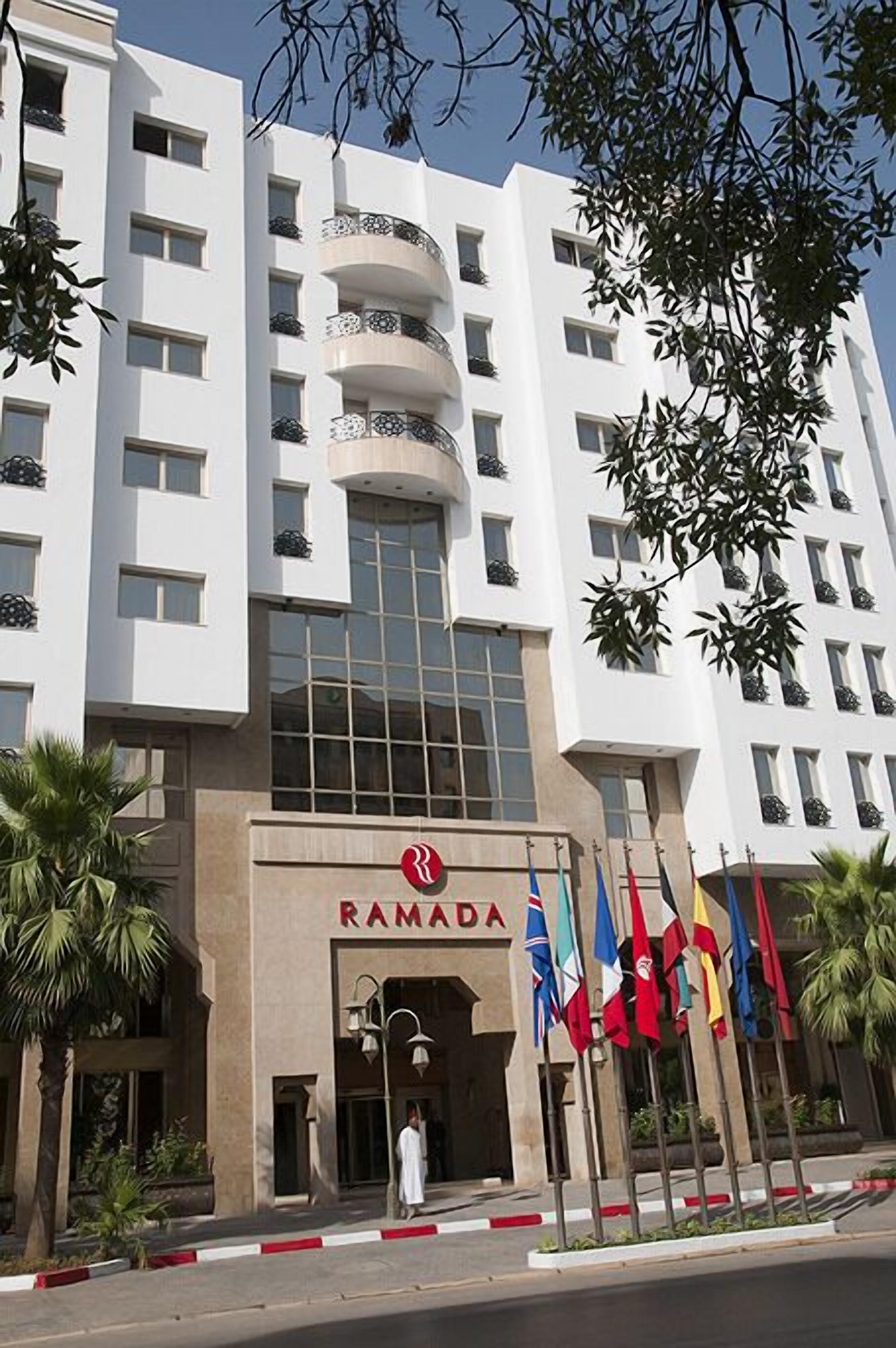 Een modern gebouw met een opvallend “RAMADA” bord, meerdere balkons en vlaggen.