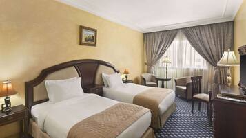 A hotel room with two beds, a desk, a chair, and a lamp.