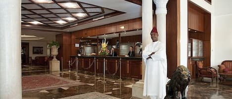 A lobby with a reception desk, a statue of a lion, and a marble floor.