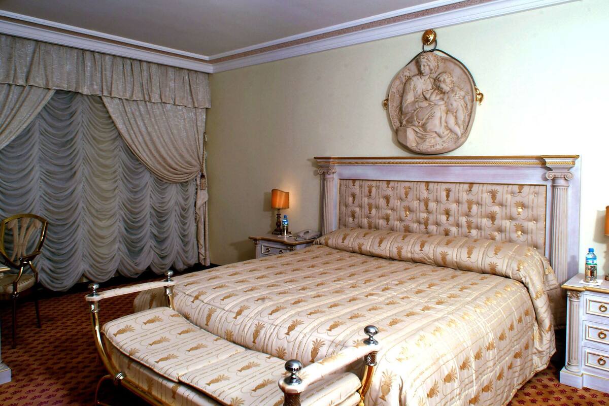 Uma cama grande com cabeceira estofada, mesa de cabeceira com abajur e uma obra de arte pendurada na parede.