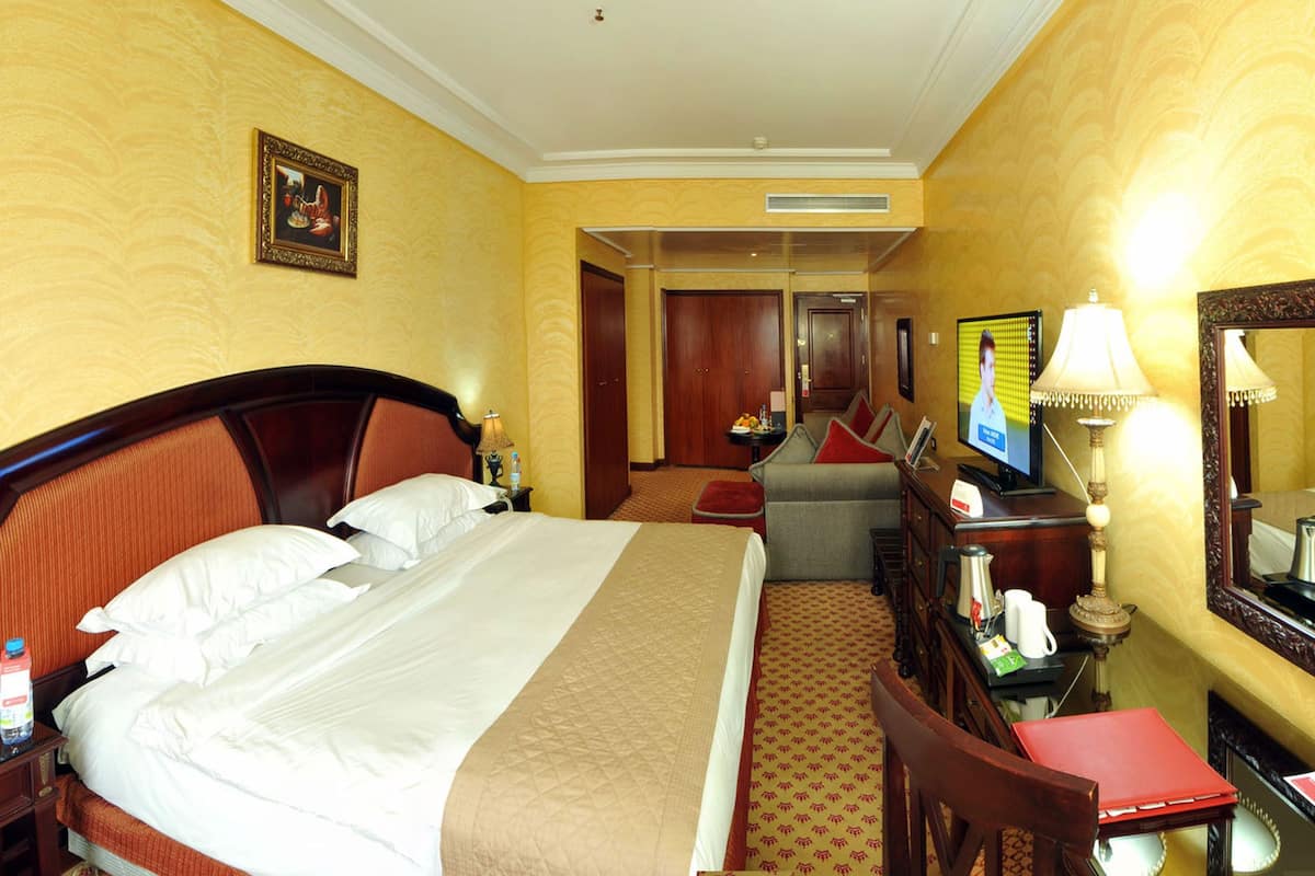 Quarto de hotel com uma cama grande, uma escrivaninha com cadeira, televisão e espelho.