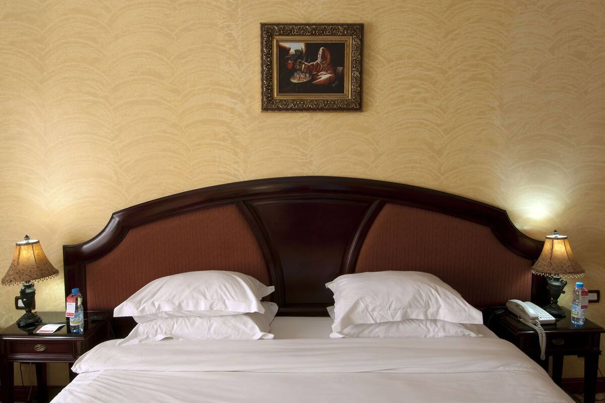 Quarto de hotel com uma cama grande, duas mesas de cabeceira, um quadro na parede e uma luminária em cada mesa.