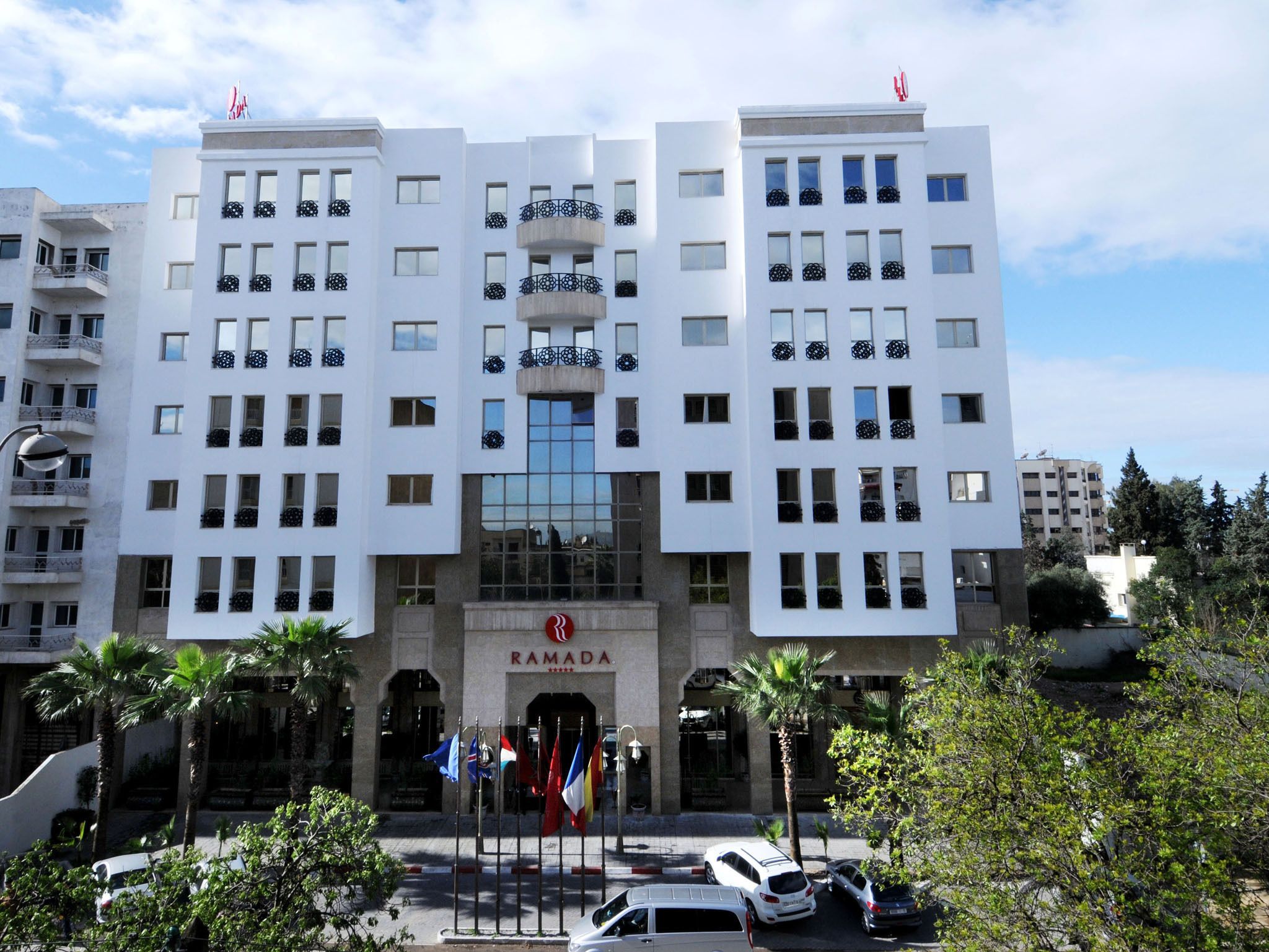 A multi-story building with a central entrance, balconies, and flags.