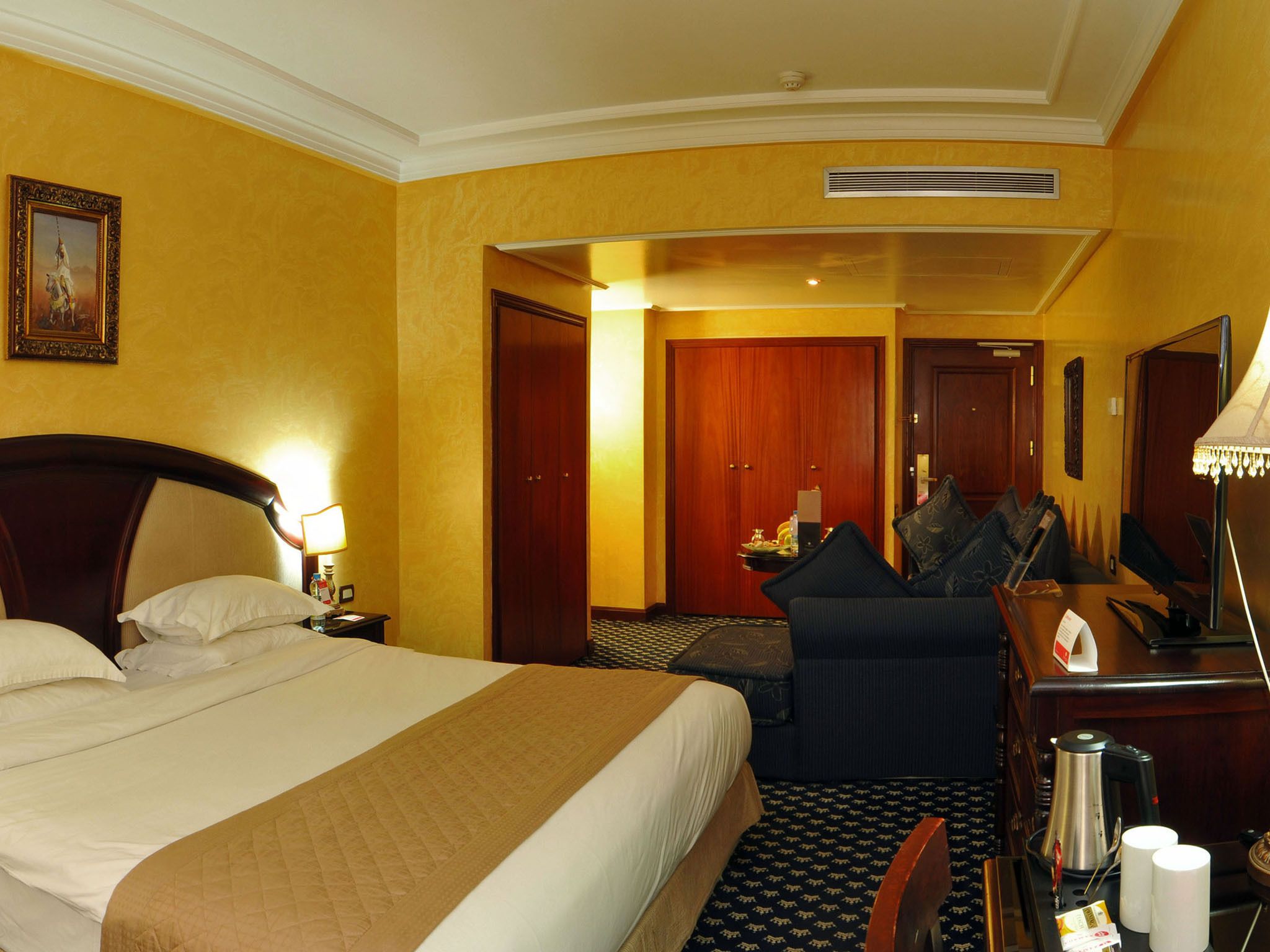 A hotel room with a large bed, a desk with a chair, a coffee maker, and a TV.