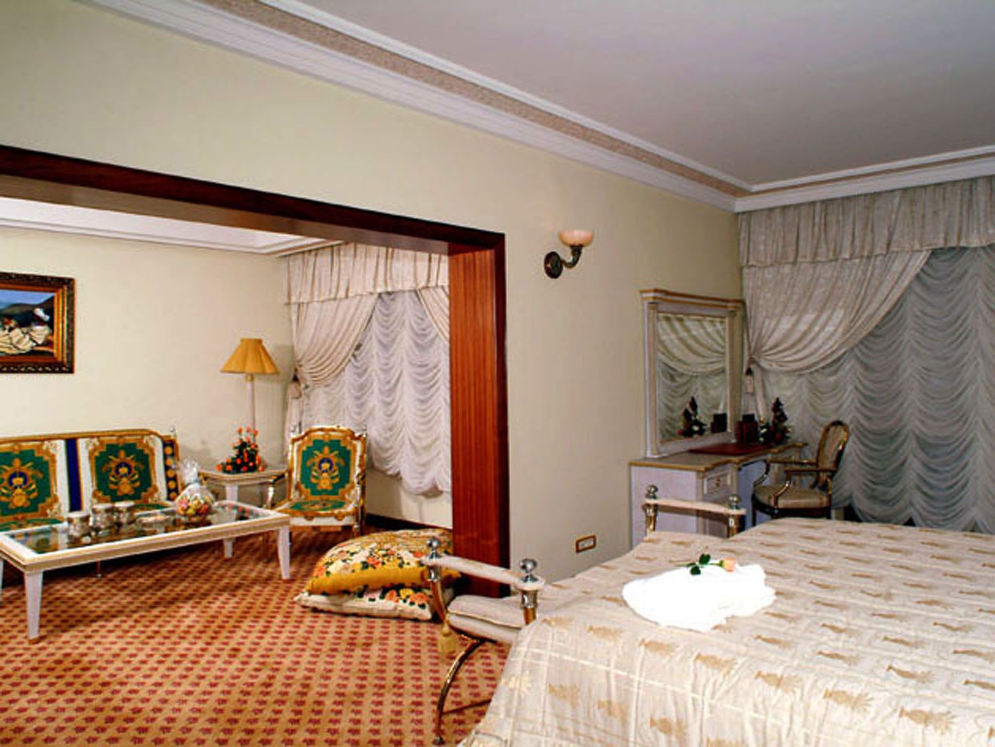 A hotel room with a bed, a desk, a chair, a sofa, and a small table with a lamp.