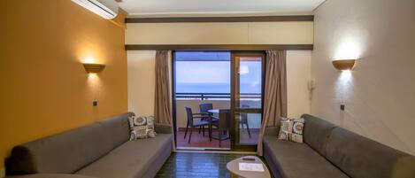 Une pièce avec deux canapés placés face à un balcon offrant une vue sur la mer. Au centre, on trouve une petite table avec une chaise.