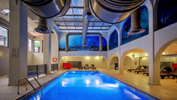 An indoor swimming pool with a view of the sky through the ceiling, lounge chairs, and a lifeguard stand. - Turial Old Town Ocean View (Albufeira)