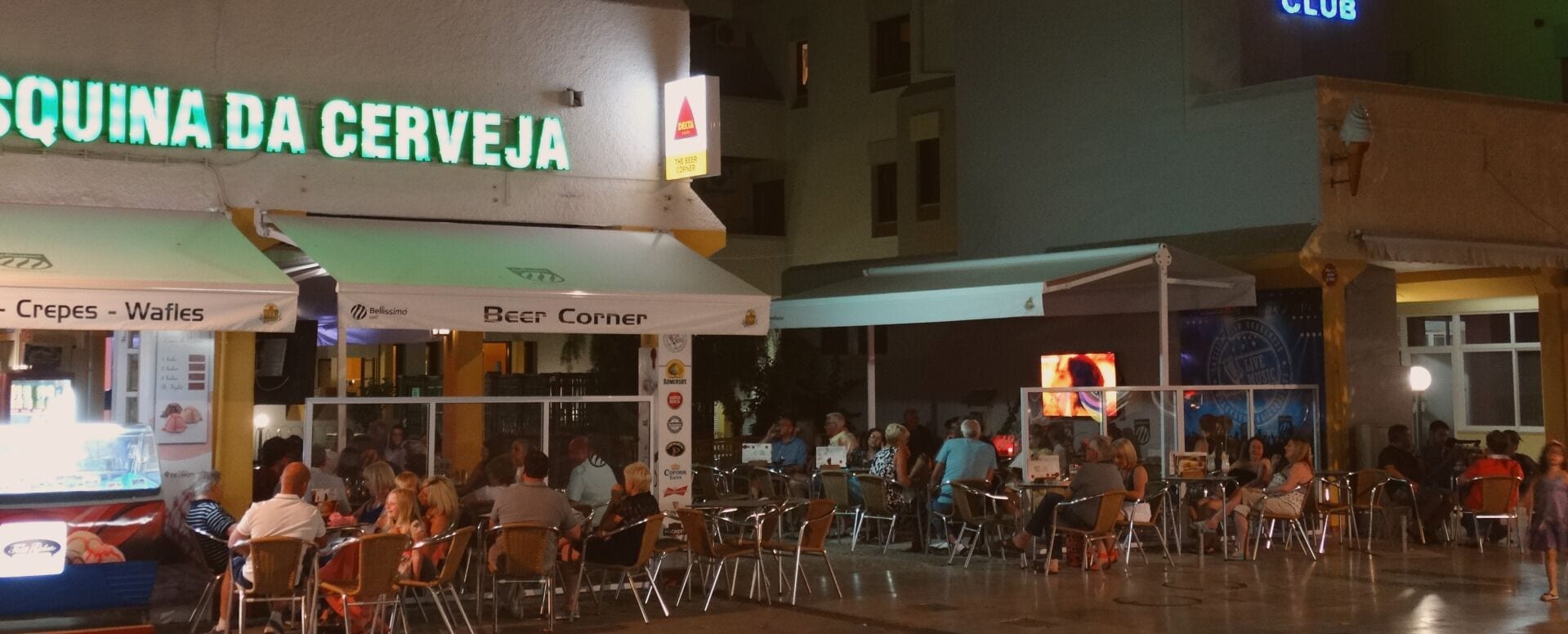 An outdoor seating area of a restaurant with a neon sign reading "QUINA DA CERVEJA" and a beer corner.