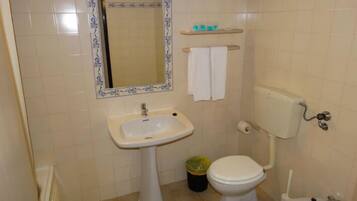 A small bathroom with a pedestal sink, toilet, bidet, and a mirror with a decorative frame.