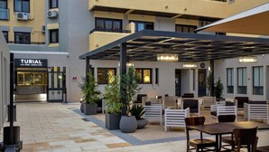 A modern outdoor seating area with tables and chairs, surrounded by potted plants, under a covered structure. - Turial Old Town Ocean View (Albufeira)