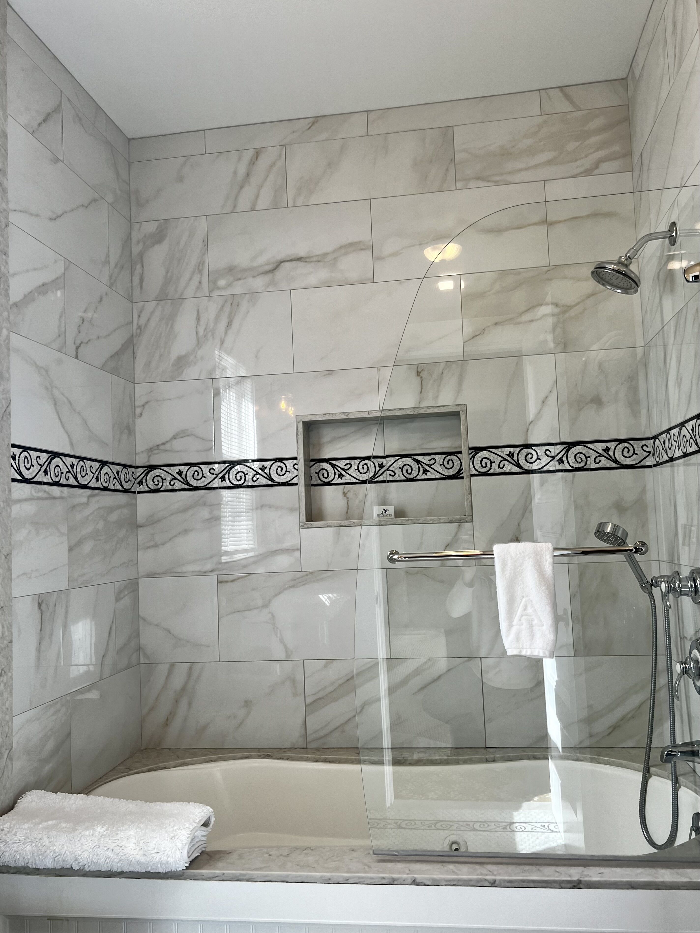 A modern bathroom with a glass-enclosed shower, a bathtub, and marble walls.