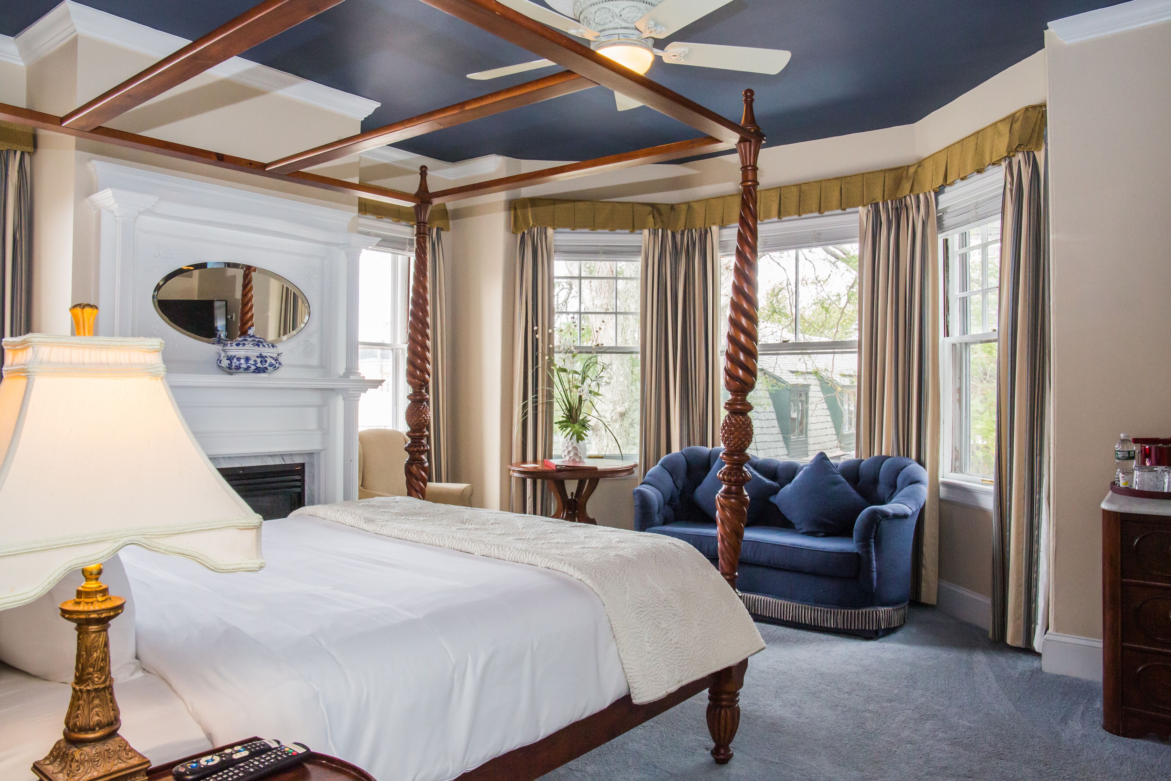 A four-poster bed with a white bedspread, a bedside lamp, and a remote control on the nightstand.