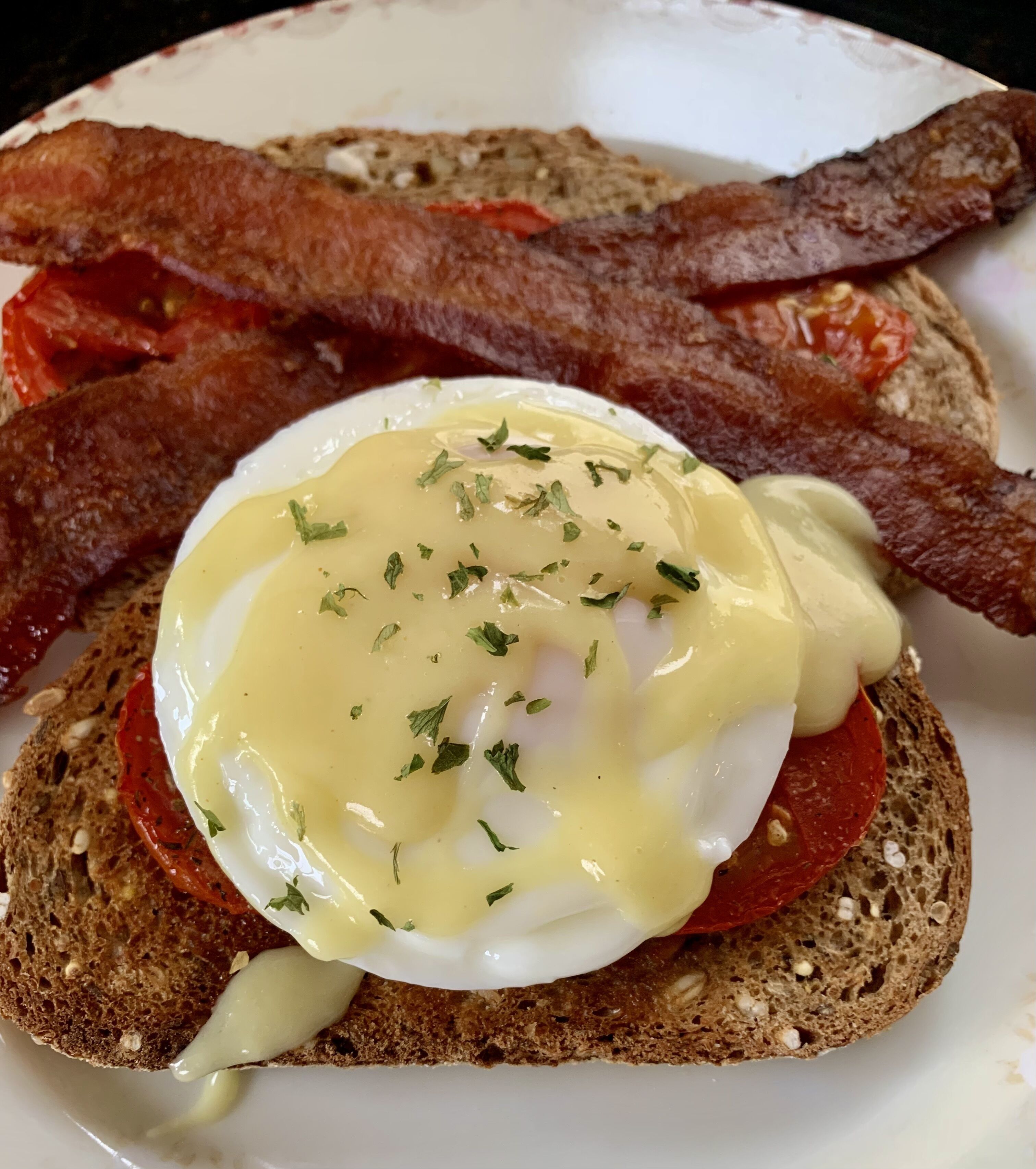 Een ontbijtbord met Eggs Benedict, spek en plakjes tomaat op volkorenbrood.