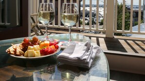 Varanda com mesa posta para dois, exibindo uma taça de vinho branco, um prato de frutas e uma toalha de papel dobrada.