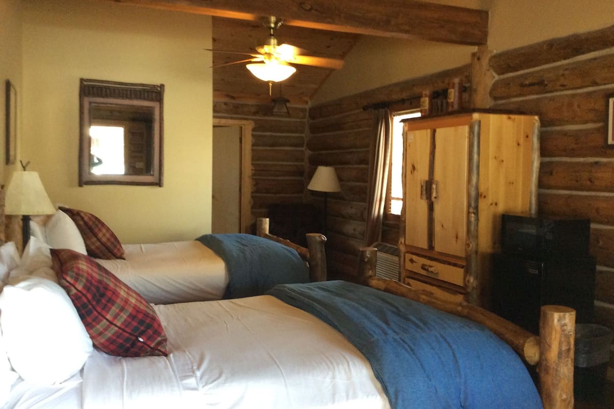 A log cabin room with two beds, a wooden wardrobe, a ceiling fan, and a mirror on the wall.