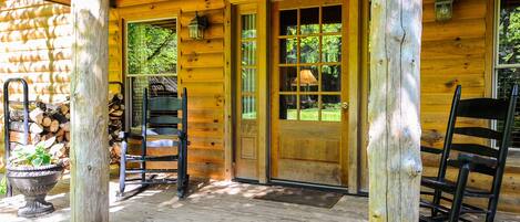 A wooden cabin with a porch, a door with glass panels, and two rocking chairs.
