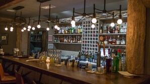 A bar area with a wooden counter, hanging light fixtures, and shelves stocked with various bottles.