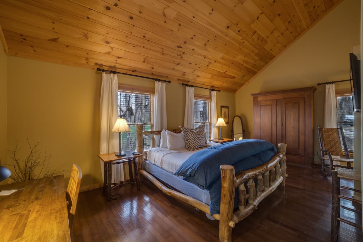 A bedroom with a wooden ceiling, a bed with a wooden headboard, a wooden desk, and a chair.