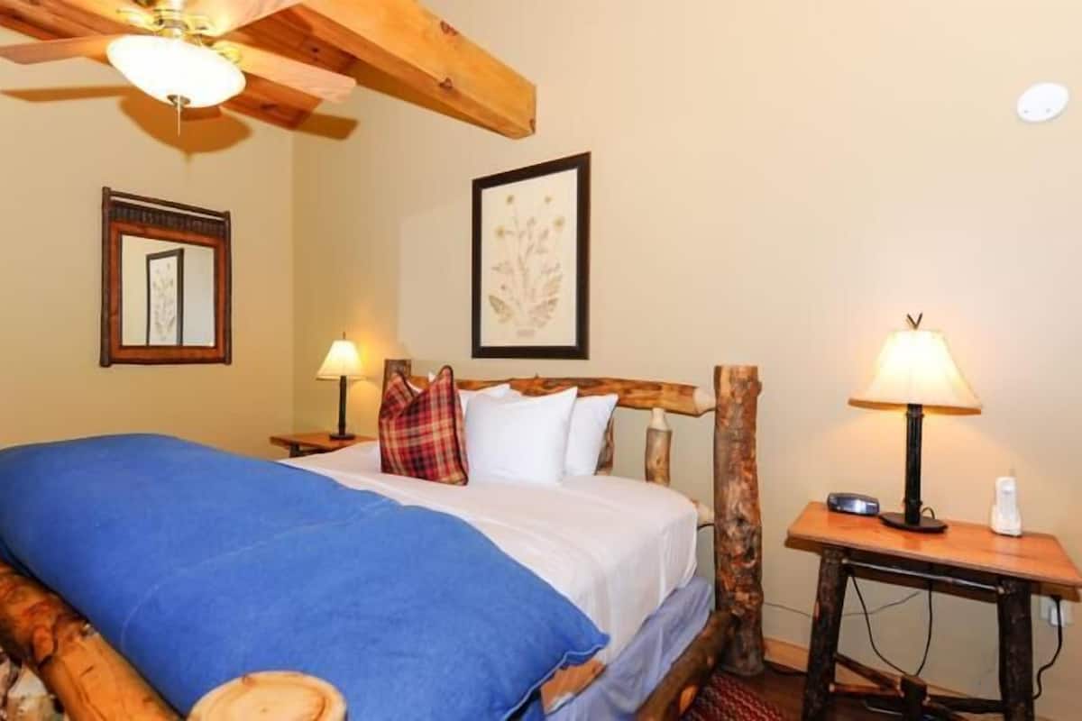 A wooden-framed bed with a blue blanket, two bedside lamps, and a framed artwork on the wall.