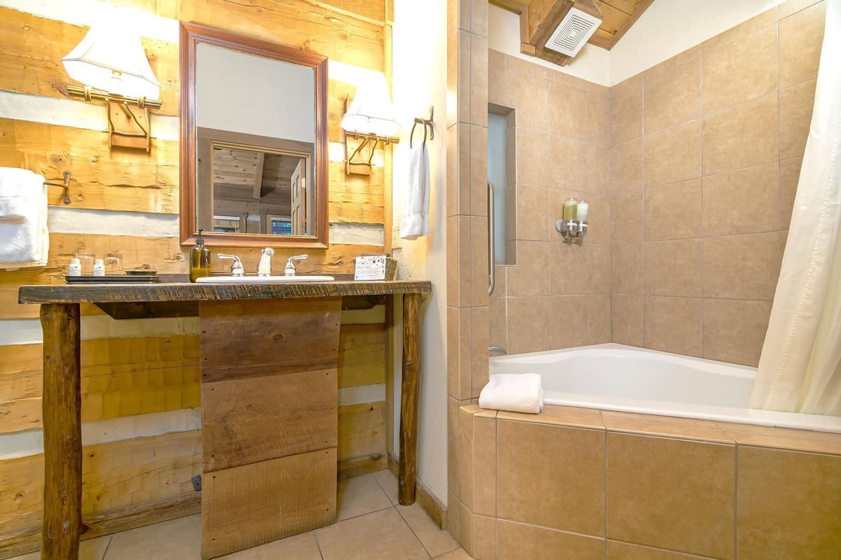A wooden bathroom with a sink, mirror, and shower.