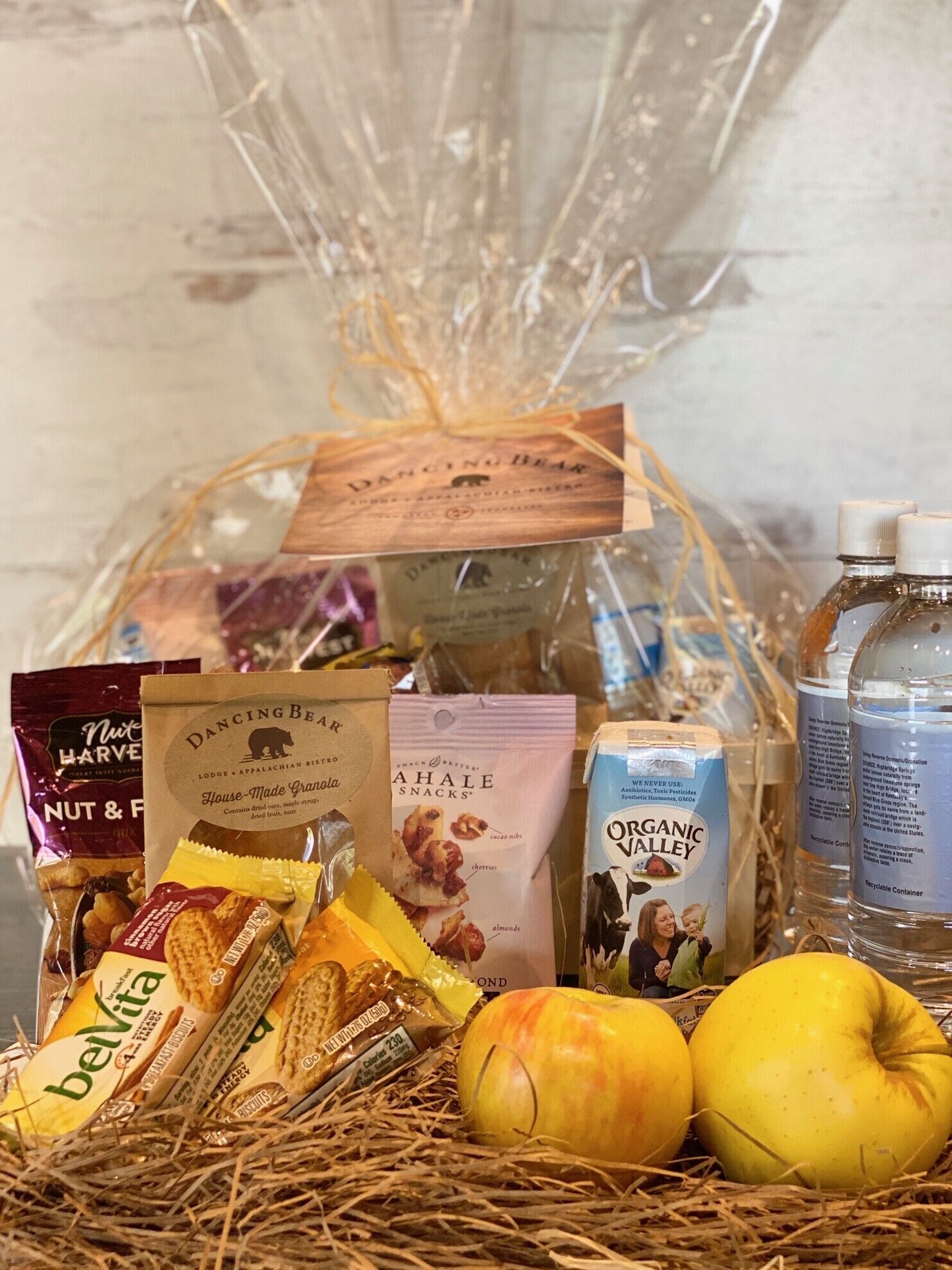 A gift basket with various items including snacks, a bottle of organic valley juice, and fresh fruits.