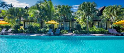 A clear blue pool with lounge chairs and yellow umbrellas, surrounded by palm trees and greenery.