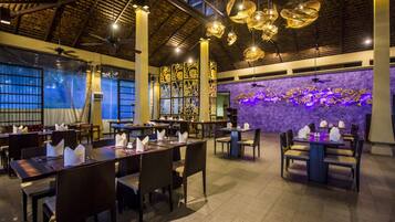 A spacious restaurant with high ceilings, exposed beams, and modern pendant lighting. Tables are neatly arranged with folded napkins and menus.