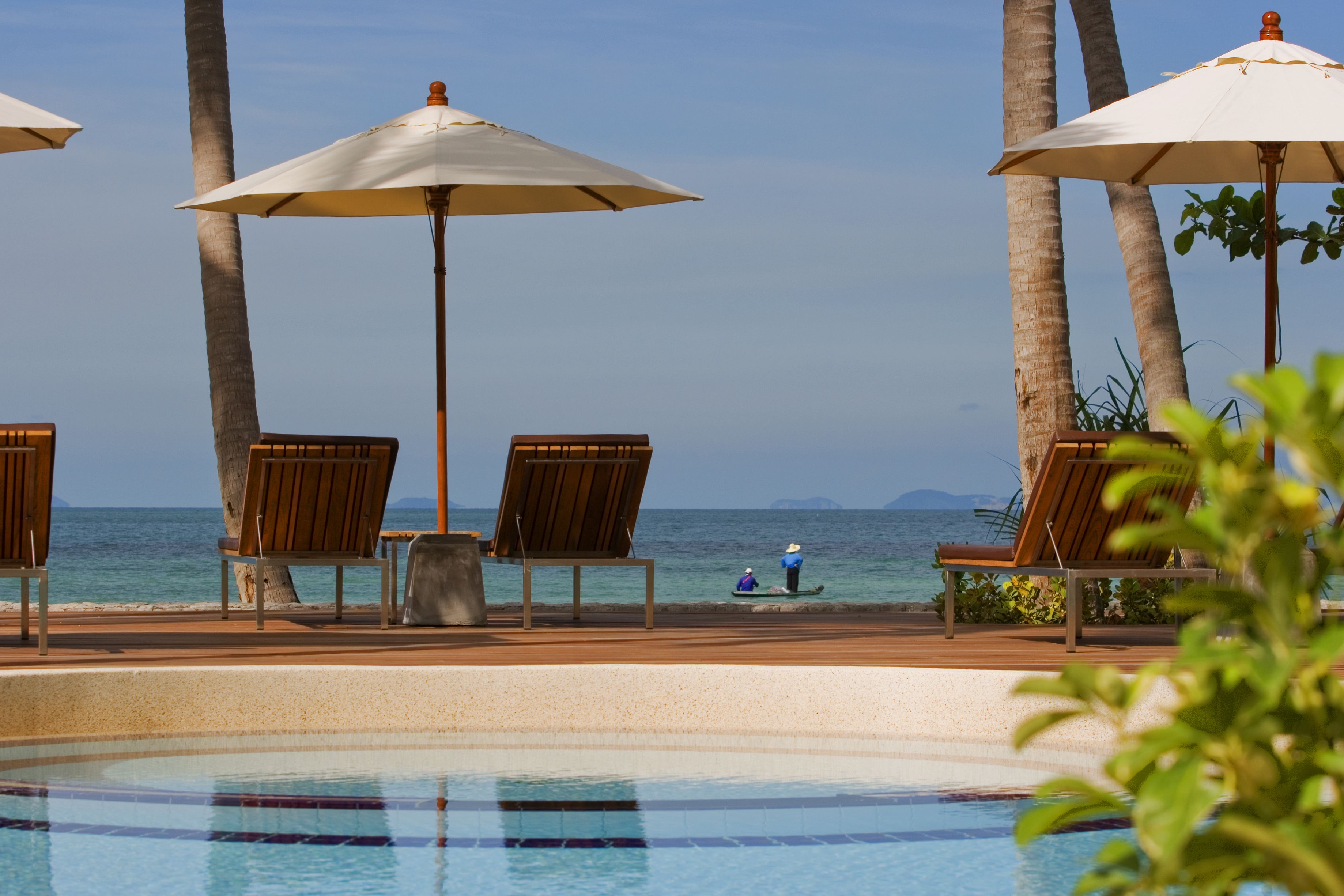 A poolside area with lounge chairs and umbrellas, overlooking the sea.