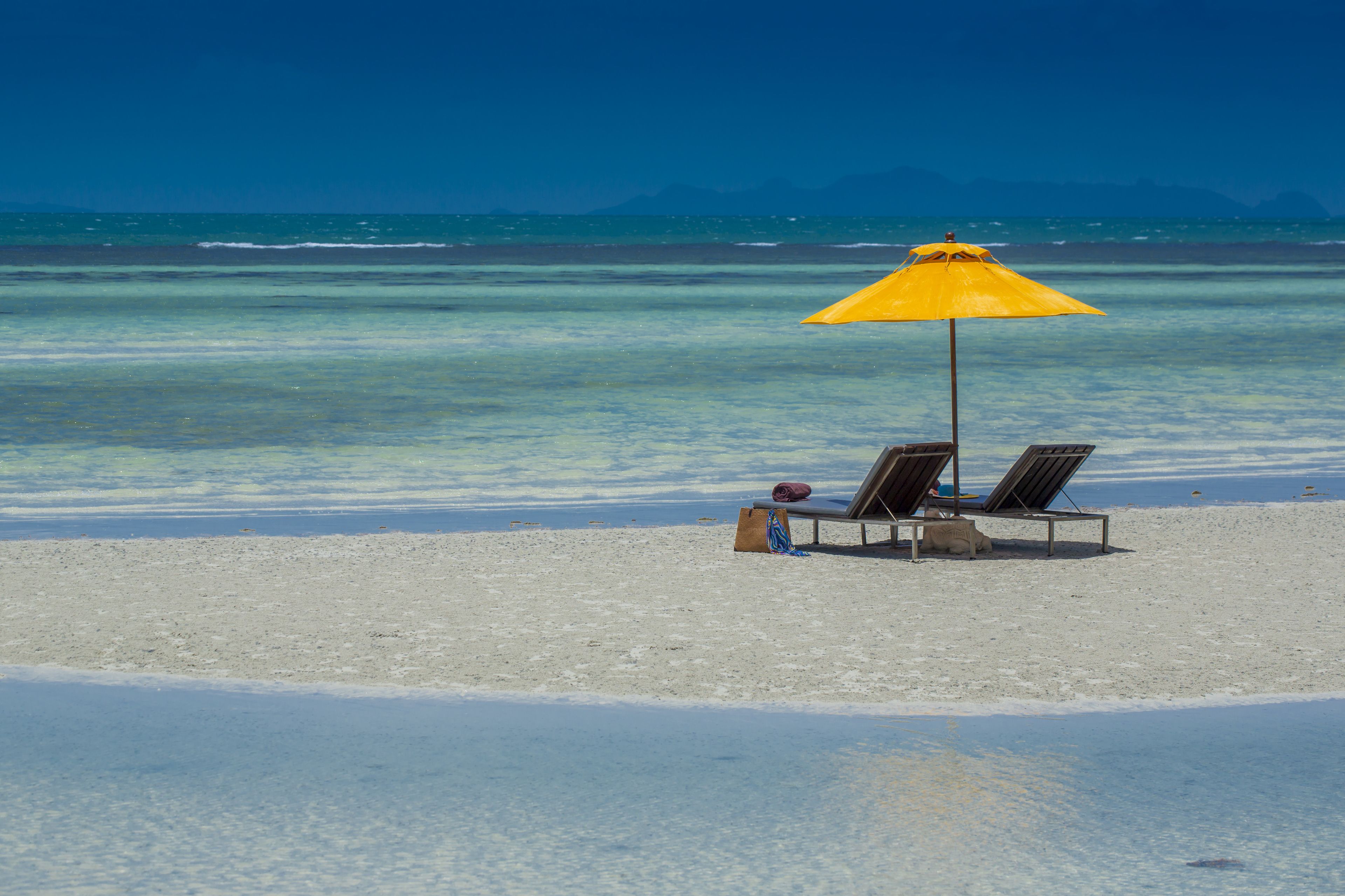 Una playa con dos sillas de playa y un paraguas amarillo.