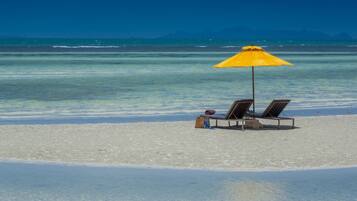 Una playa con dos sillas de playa y un paraguas amarillo.