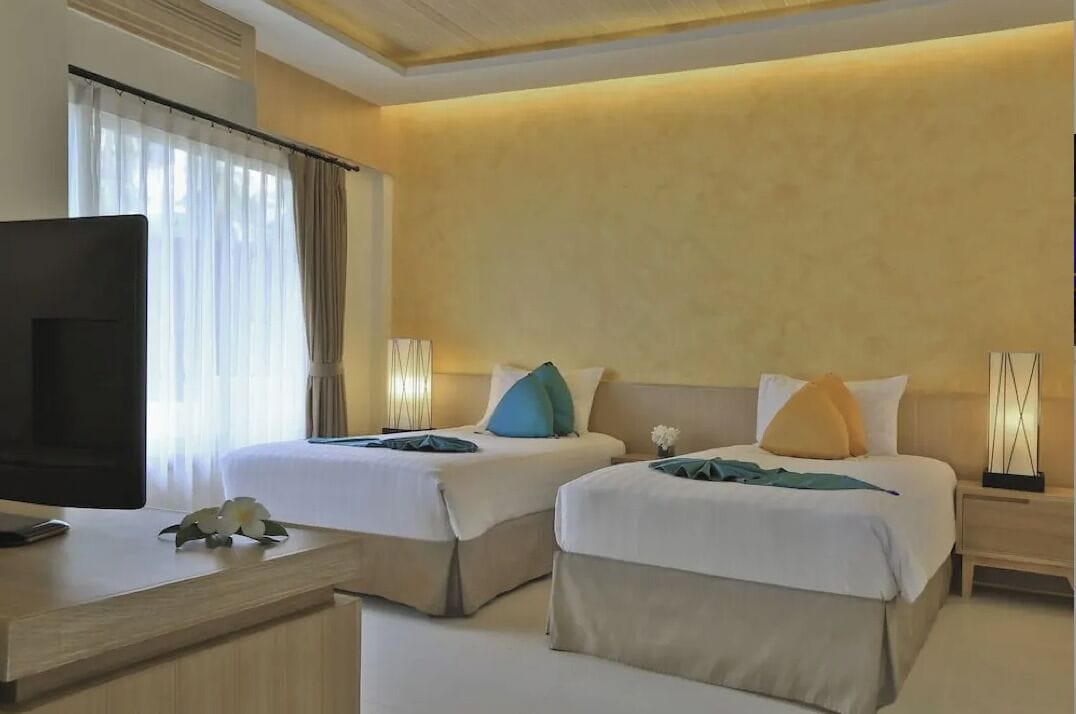Habitación de hotel con dos camas, televisión y escritorio con una flor.