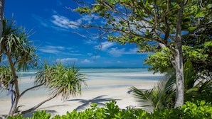 A beach with clear blue water, white sand, and lush green foliage. - TUI BLUE The Passage Samui Pool Villas with Private Beach Resort (Koh Samui)