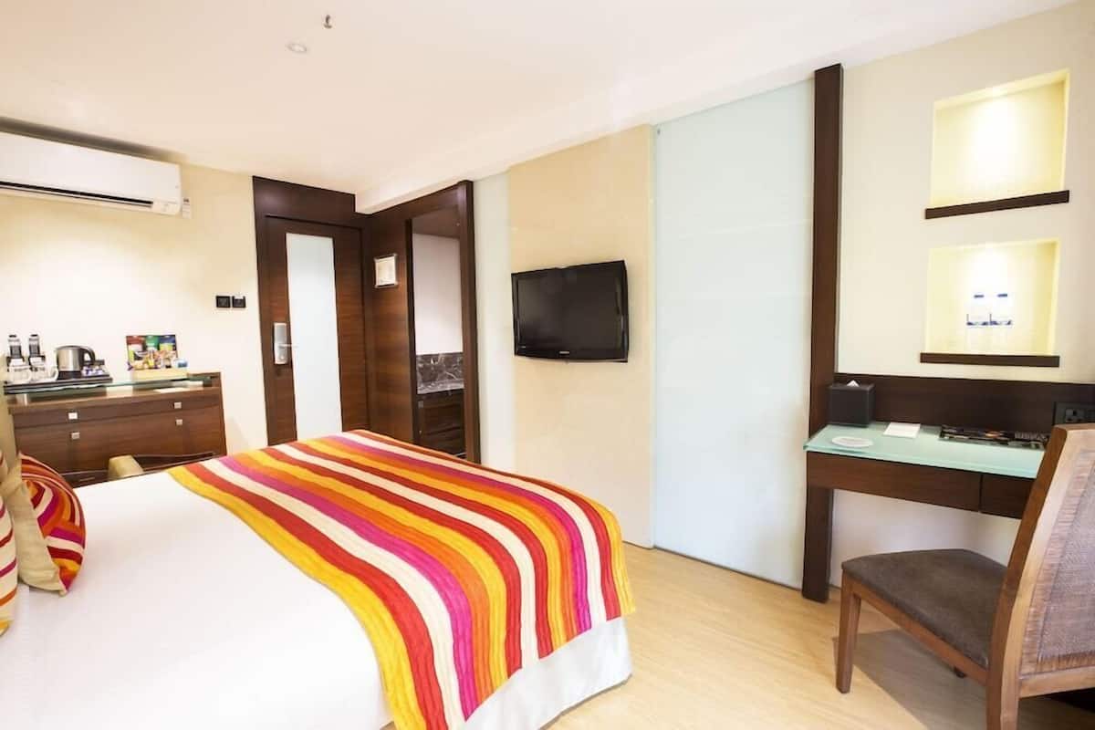 Une chambre d’hôtel équipée d’un lit, d’un bureau, d’une chaise, d’une télévision et d’un mini-bar.