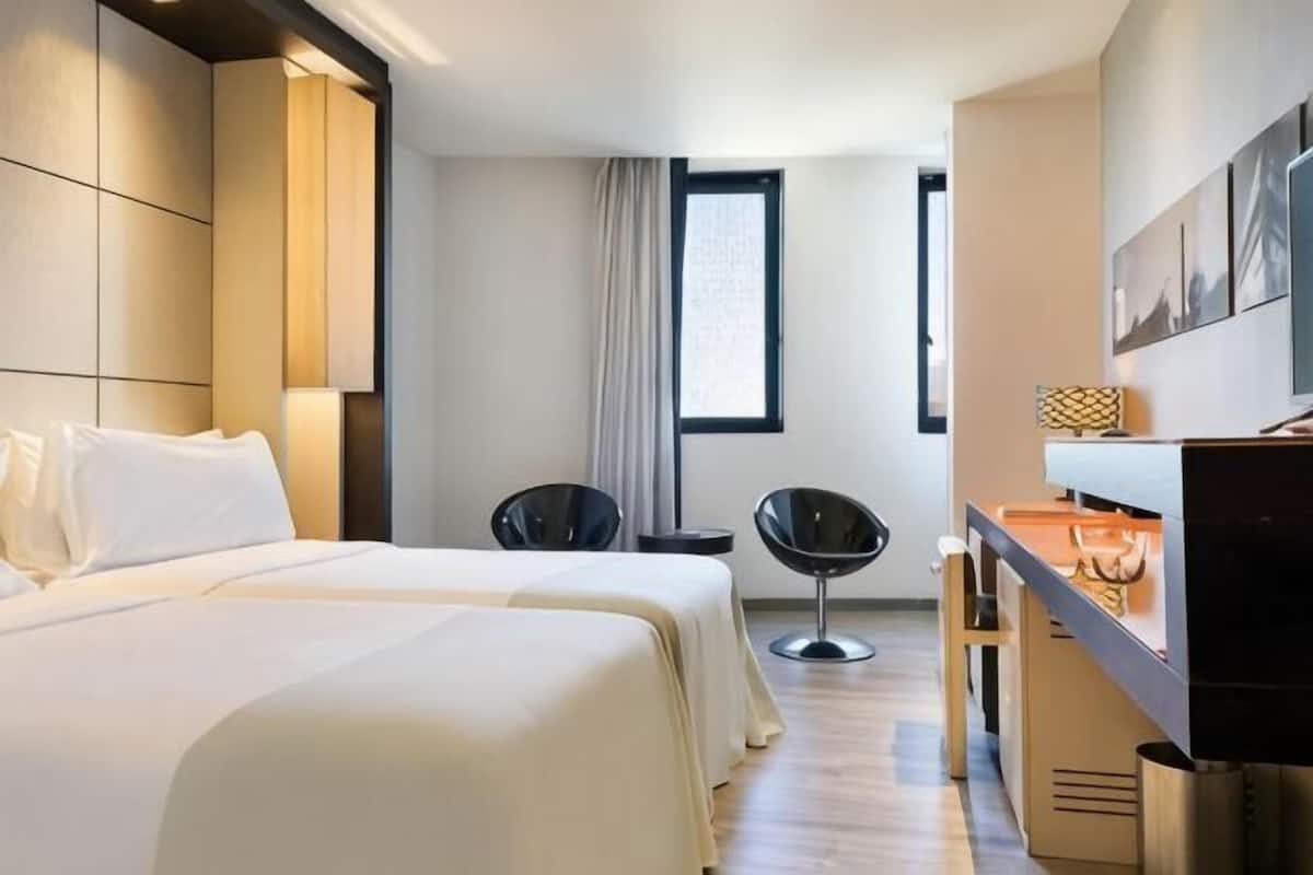 Une chambre d’hôtel avec deux lits, un bureau, une chaise, une télévision et une fenêtre.