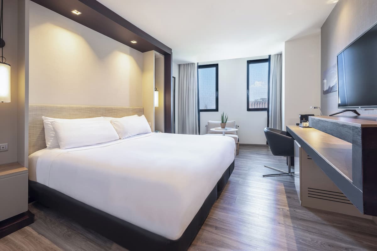 Une chambre d’hôtel moderne dotée d’un grand lit, d’un bureau, d’une télévision à écran plat et d’une petite table agrémentée d’une plante.