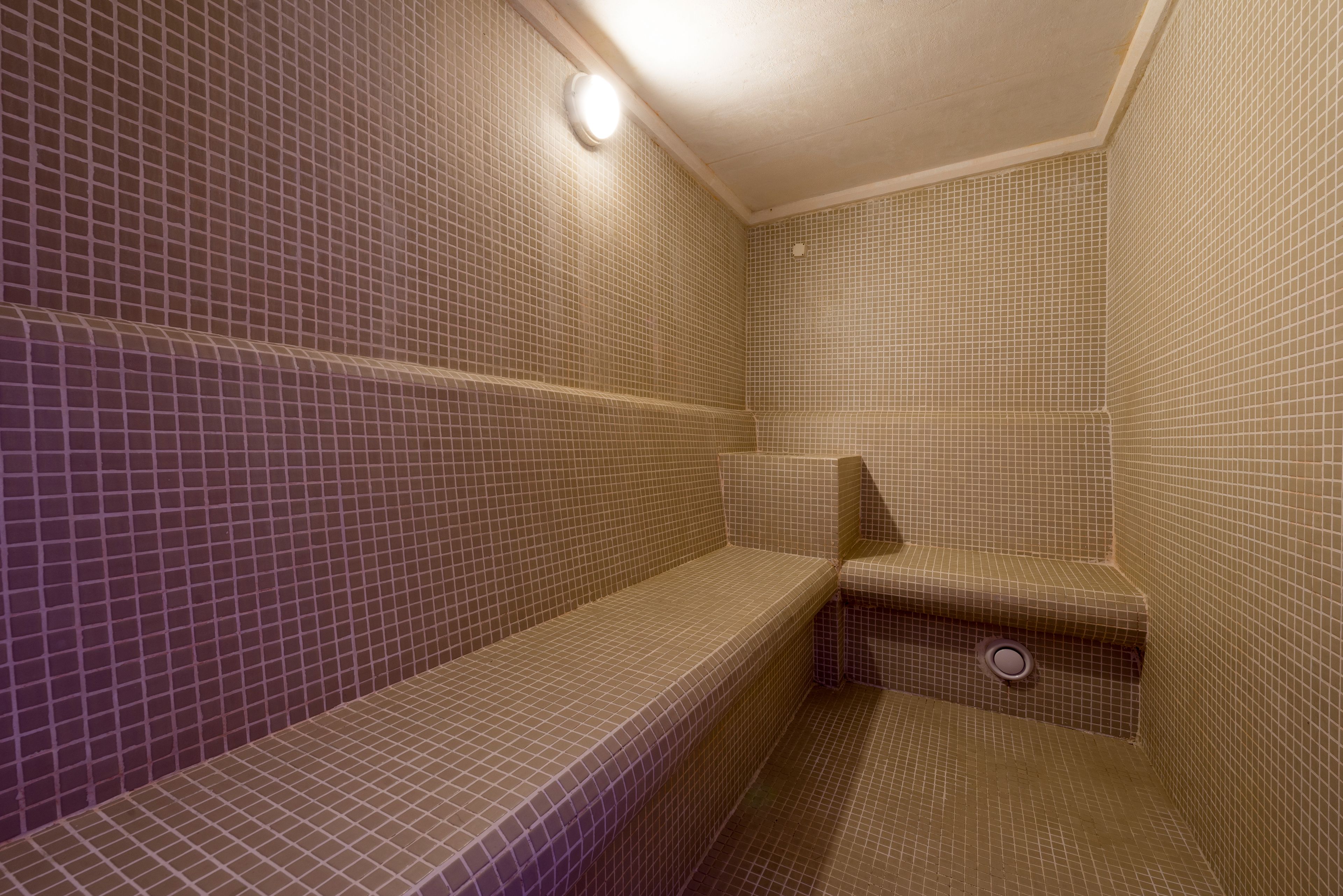 A small, tiled bathroom with a bench and a sink.