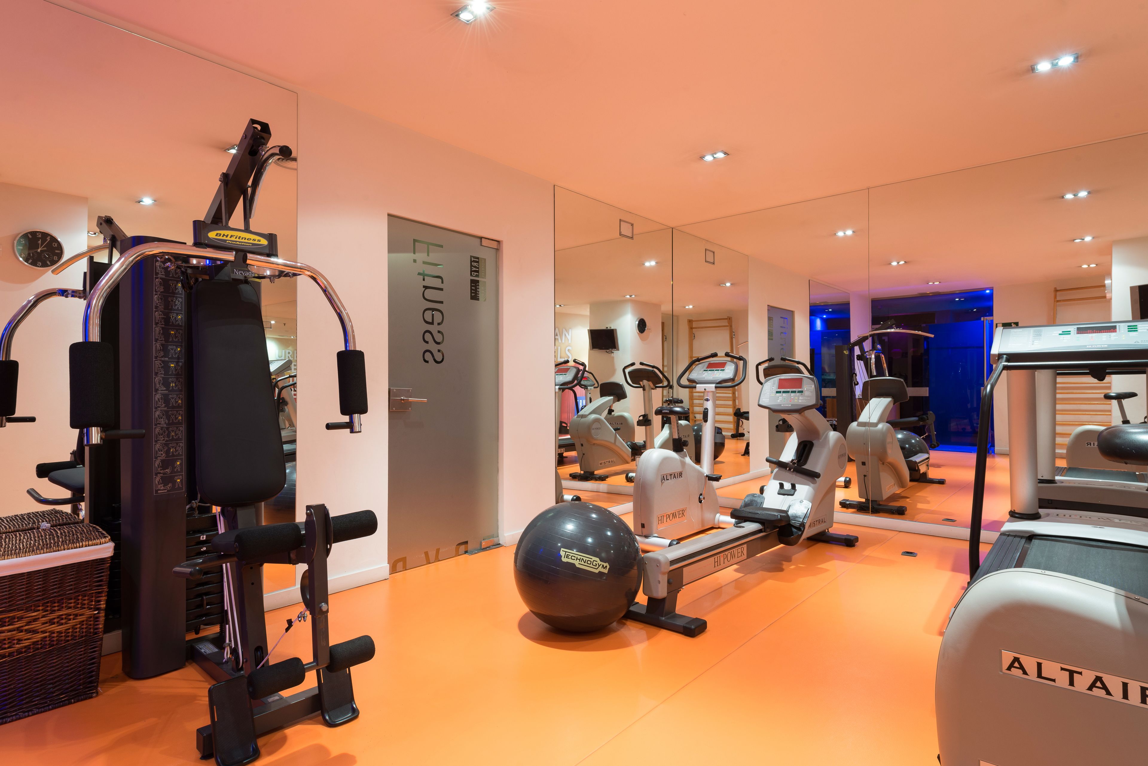 A gym with various exercise equipment, including a rowing machine, elliptical, and stationary bikes.