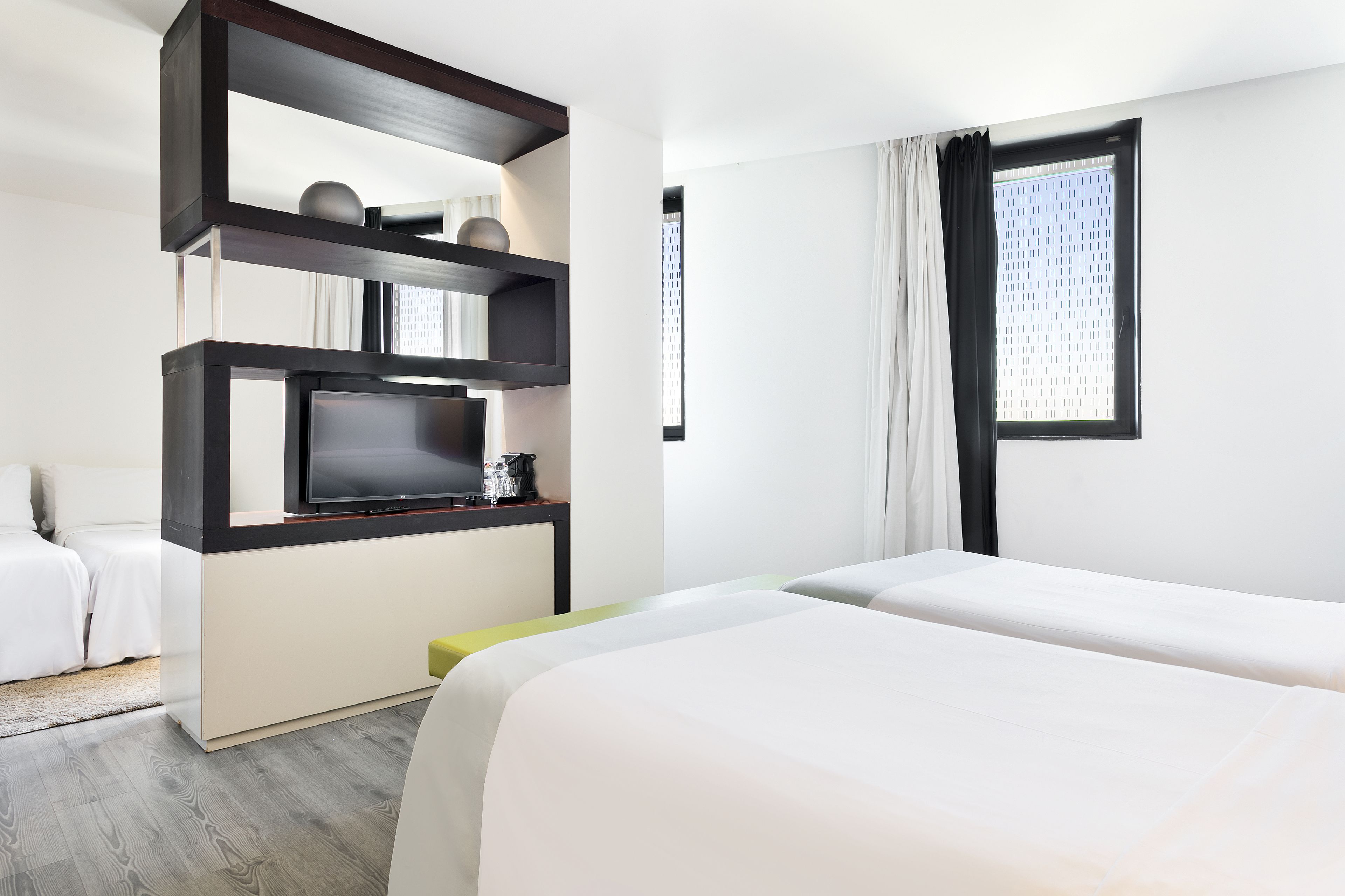 Una habitación de hotel con cama, televisión, cafetera y ventana con cortinas.