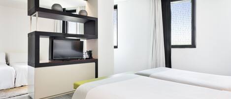 Una habitación de hotel con cama, televisión, cafetera y ventana con cortinas.