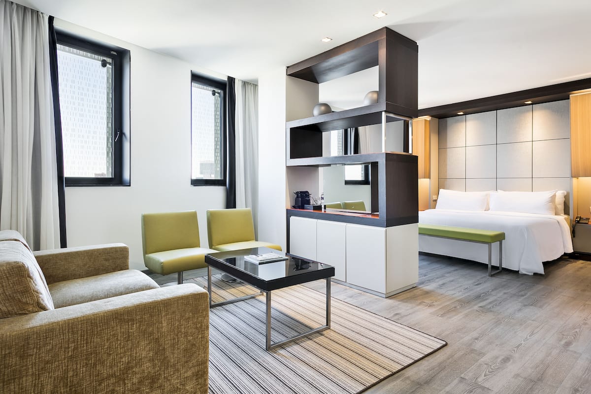 Une chambre d’hôtel moderne, équipée d’un canapé, d’une petite table, d’un lit et d’une bibliothèque intégrée.