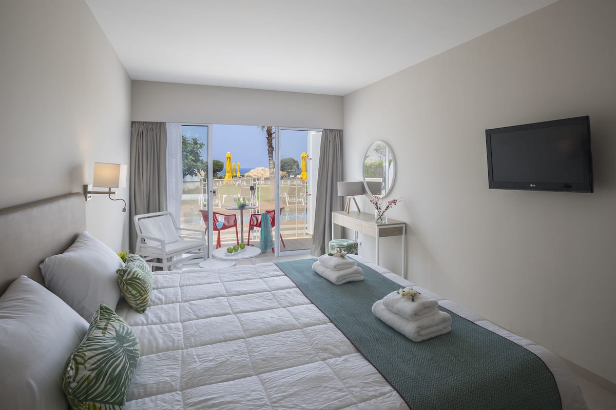 Une chambre d’hôtel avec un grand lit, une télévision, un bureau avec une chaise et une vue sur la plage.