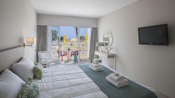 Un cuarto de hotel con una cama grande, televisión, escritorio con silla y vista a la playa.