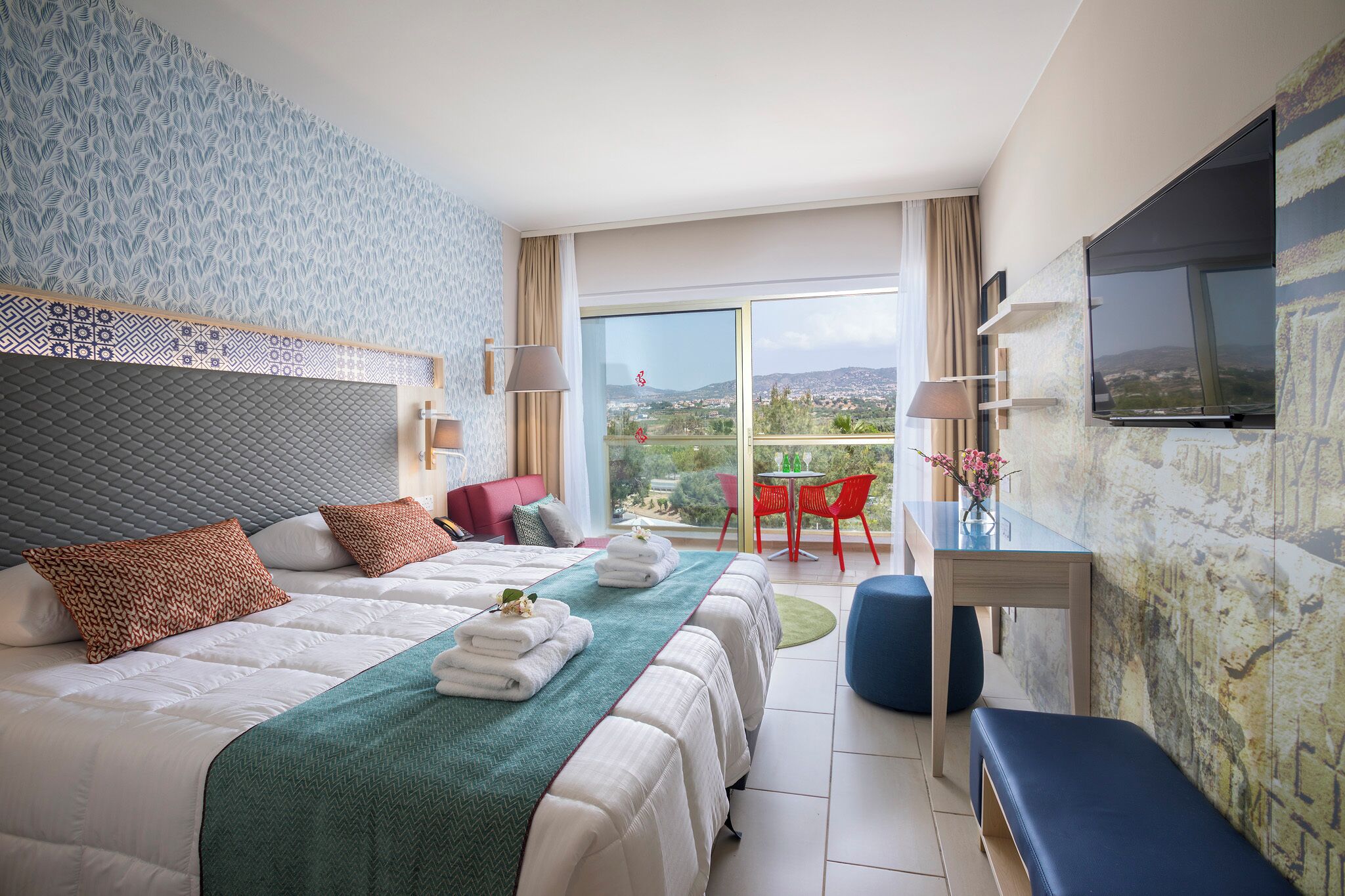 Ein Hotelzimmer mit Bett, Schreibtisch, Fernseher und einem Balkon mit Blick.